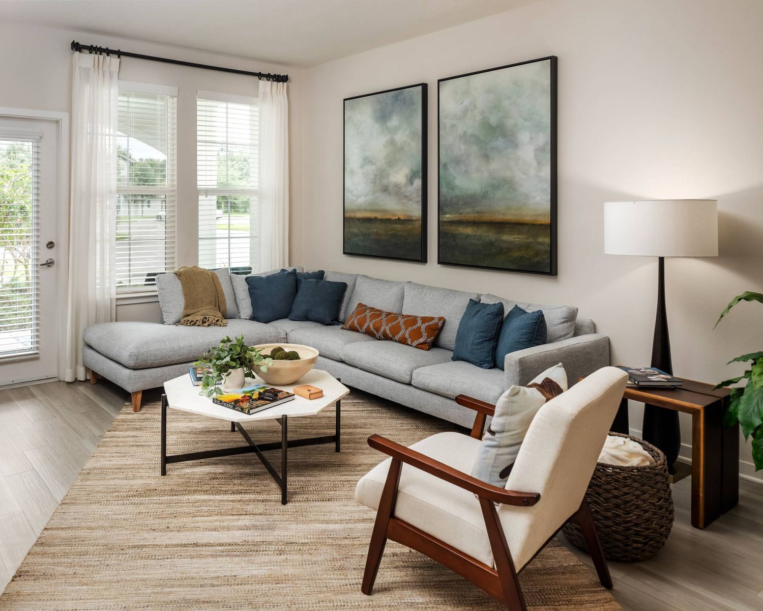 Shadetree Apartments with Modern living room with gray sectional sofa, armchair, coffee table, large windows, and landscape art on the wall.