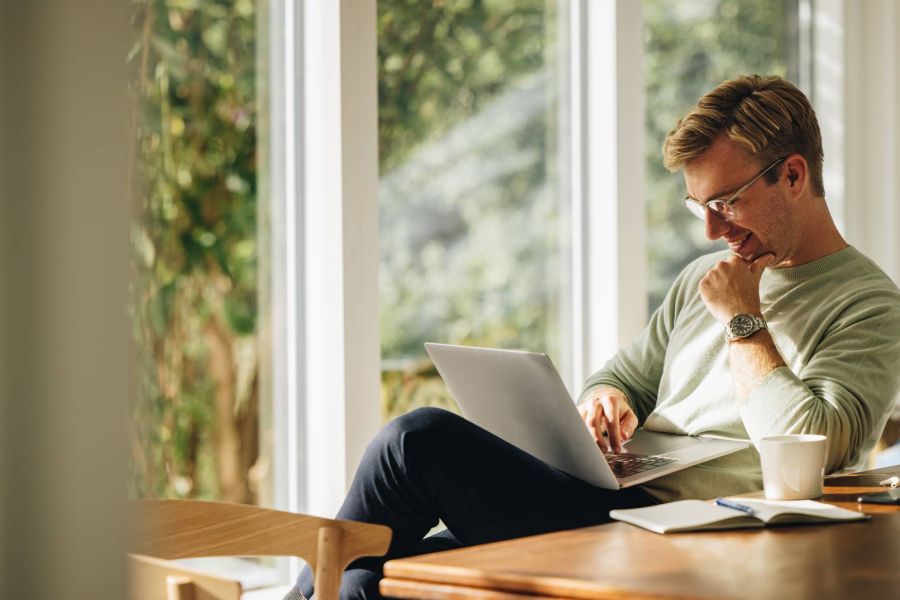 Shadetree Apartments with Man sitting at a table by a window, using a laptop with a notebook, pen, and coffee cup nearby.
