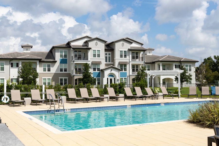 Shadetree Apartments with Modern apartment building with lounge chairs beside a swimming pool under a partly cloudy sky.