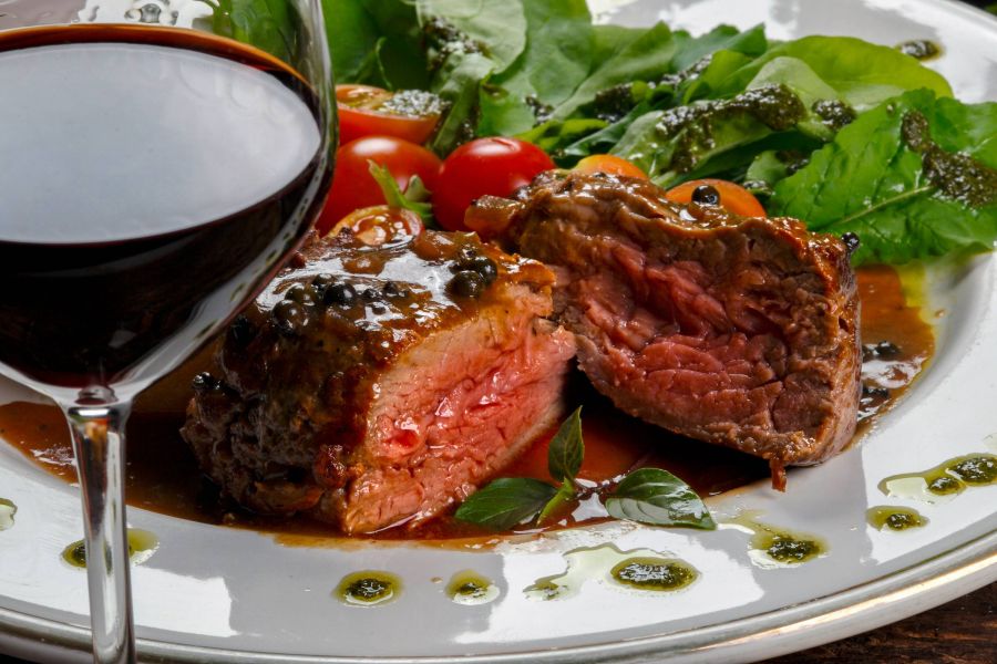 Shadetree Apartments near The Capital Grille with a close up of a filet mignon steak dinner and salad with dark red wine