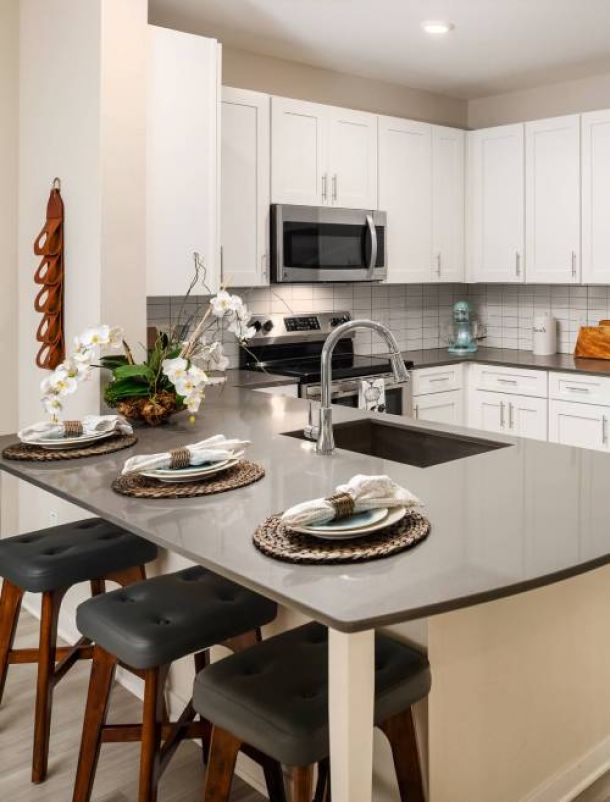 Shadetree Apartments with Modern kitchen with white cabinets, gray countertop, and place settings for three at the island.