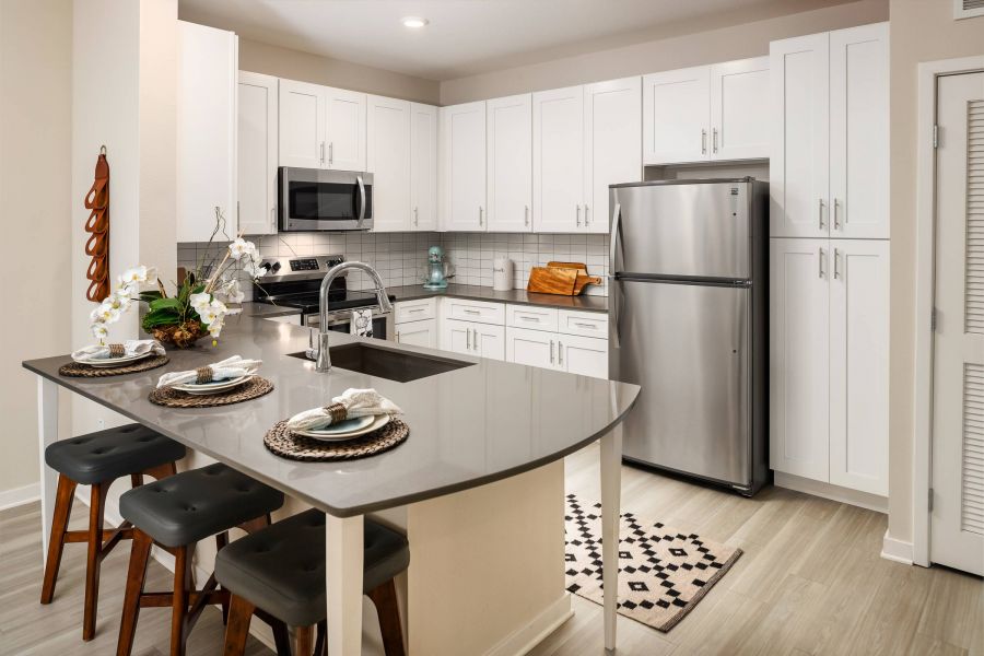 Shadetree Apartments with Modern kitchen with white cabinets, stainless steel appliances, and a gray island set for three people.