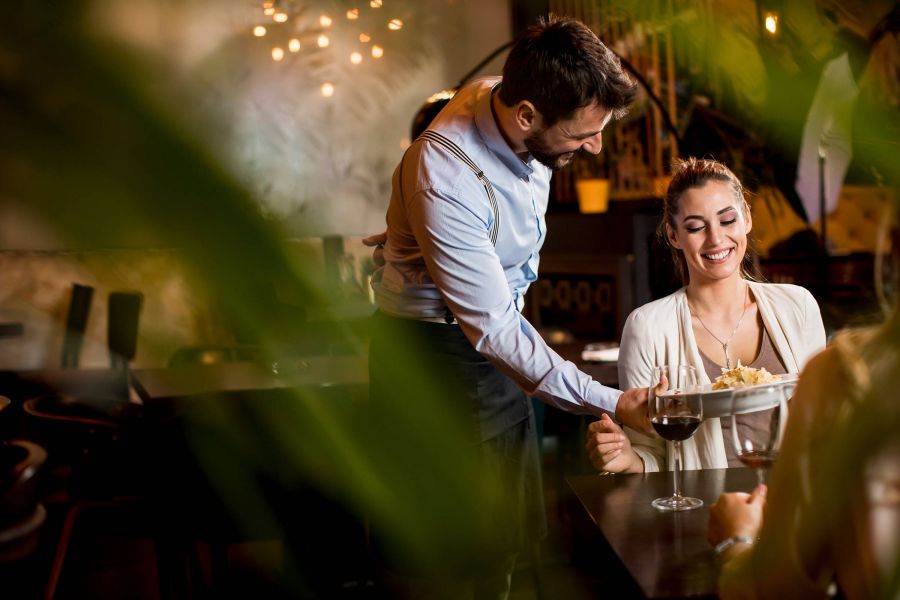 Shadetree Apartments with Two smiling young female friends at a restaurant with waiter serving dinner