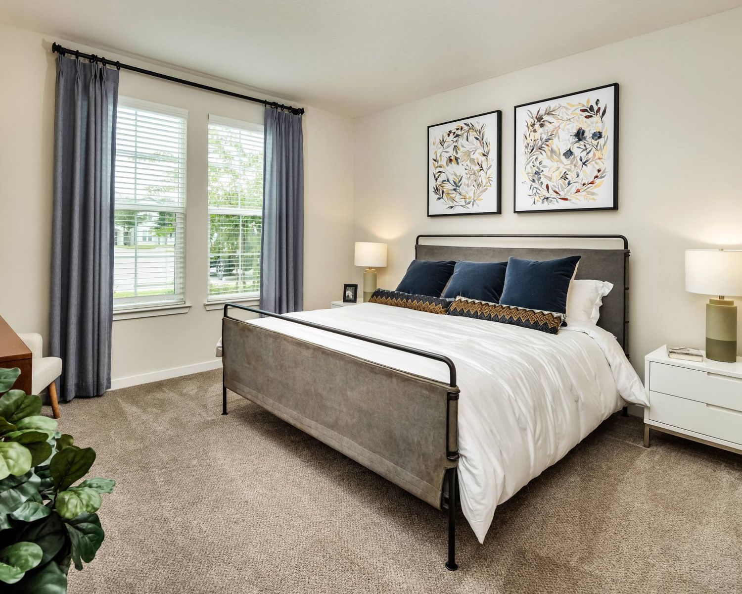 Shadetree Apartments with Modern bedroom with a metal bed, white bedding, two nightstands, and botanical art above the bed.