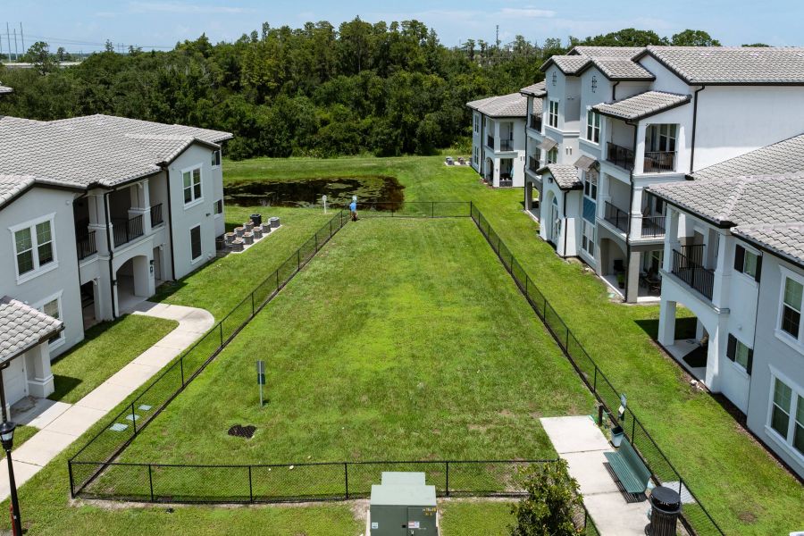 Shadetree Apartments with Fenced grassy area between two apartment buildings with a sidewalk, benches, and trees in the background.