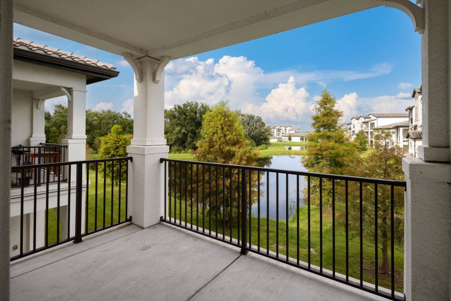 Shadetree Apartments with View from a covered balcony overlooking a pond, trees, and nearby apartment buildings under a blue sky.