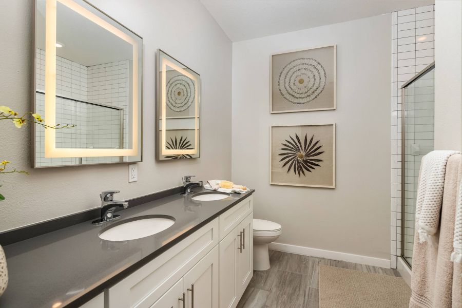 Shadetree Apartments with Modern bathroom with double sinks, illuminated mirrors, wall art, and a glass shower.