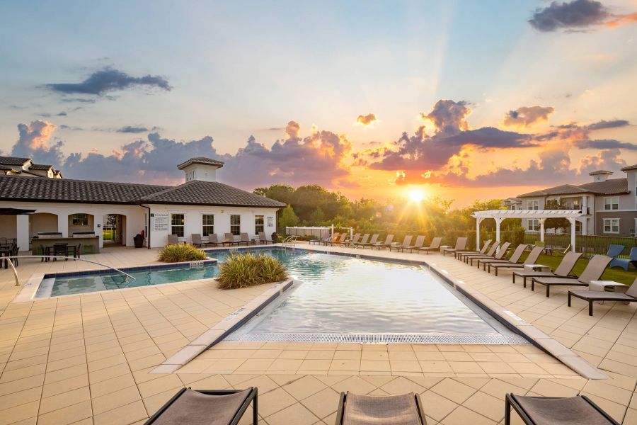 Shadetree Apartments with Outdoor pool with lounge chairs and a building, at sunset with vibrant clouds and sun rays in the sky.