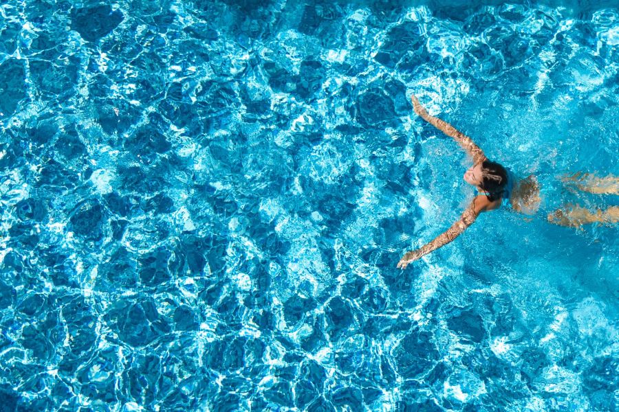 Shadetree Apartments with A person swims on their back in a bright blue swimming pool, arms stretched out wide.