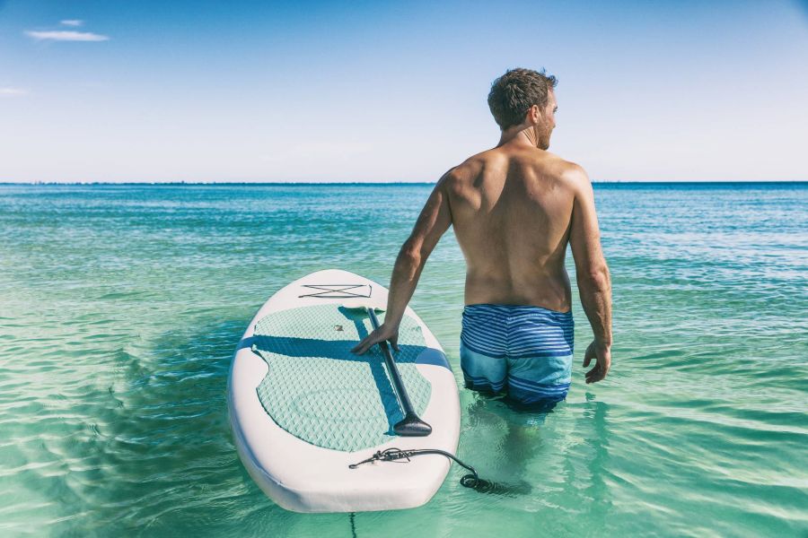 Shadetree Apartments with a man taking a SUP paddle board out in tropical water to do watersports