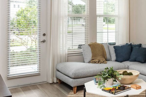 Shadetree Apartments with Bright living room with a gray sectional sofa, coffee table, and large windows with white curtains and blinds.
