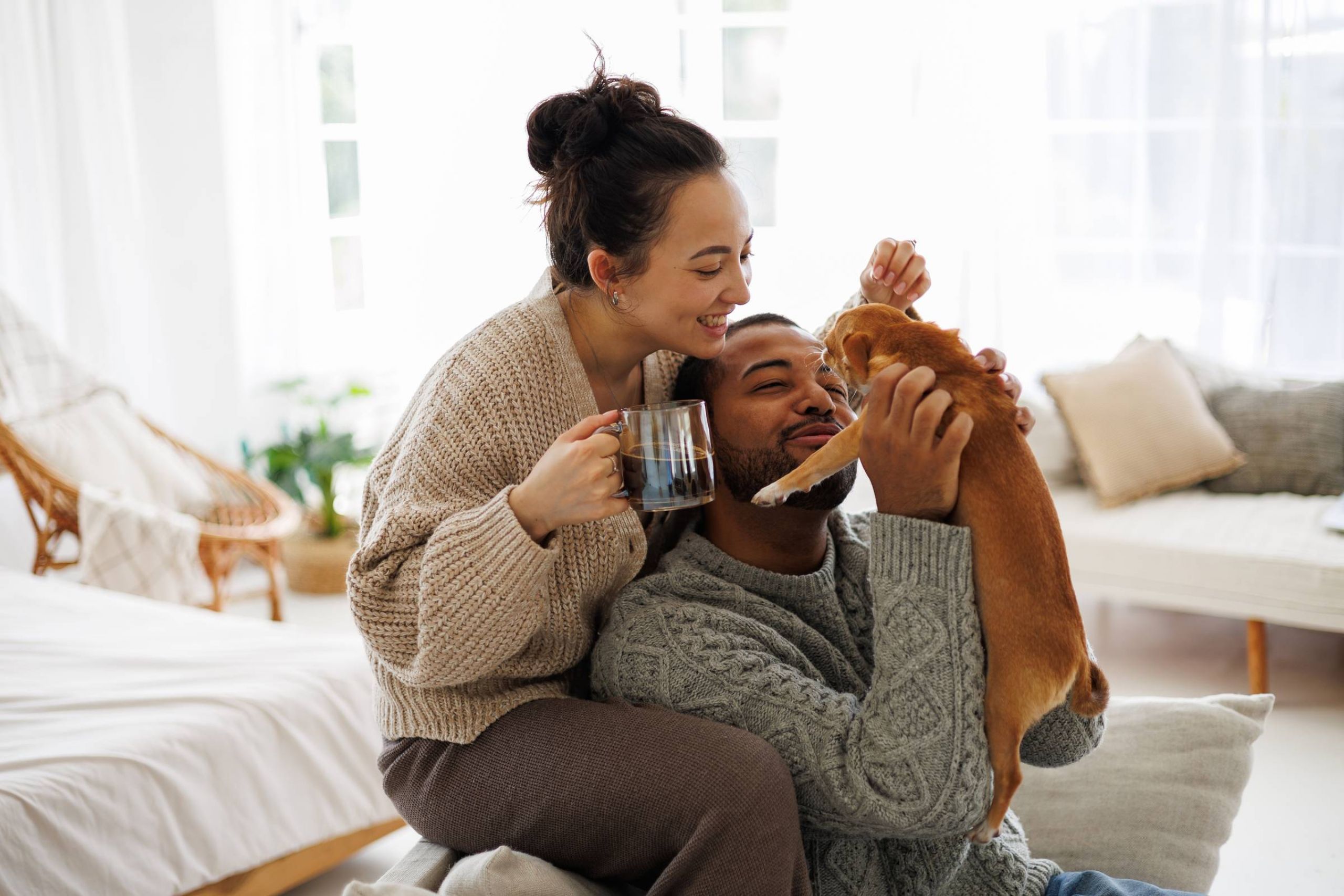 Shadetree Apartments with a smiling couple sitting close together in their living room and holding and admiring their small puppy 