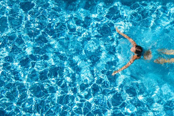 Shadetree Apartments with A person swims on their back in a bright blue swimming pool, arms stretched out wide.